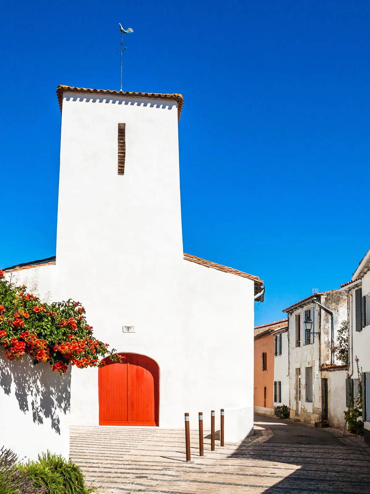 The church of Les Portes-en-Ré, white facade and red door, flowered lane